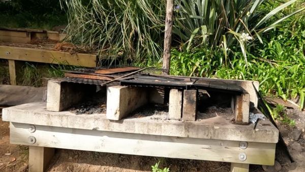 This image shows three brick barbeques joined together and sitting on a wooden frame about waste height. Sitting on top of the wooden frame are five bricks laying horizontally where coal can be stacked and lit. These bricks also divide the barbeque into three. Each barbeque grid plate sits atop of these horizontal bricks.