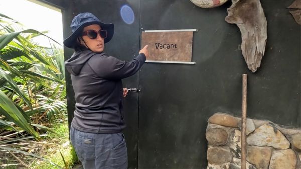 In this image, Vicki is pointing to the wooden in use sign of the bath house which is showing that the bath house is vacant.